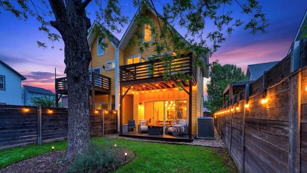 Una casa con porche cubierto, mobiliario exterior y luces colgantes.