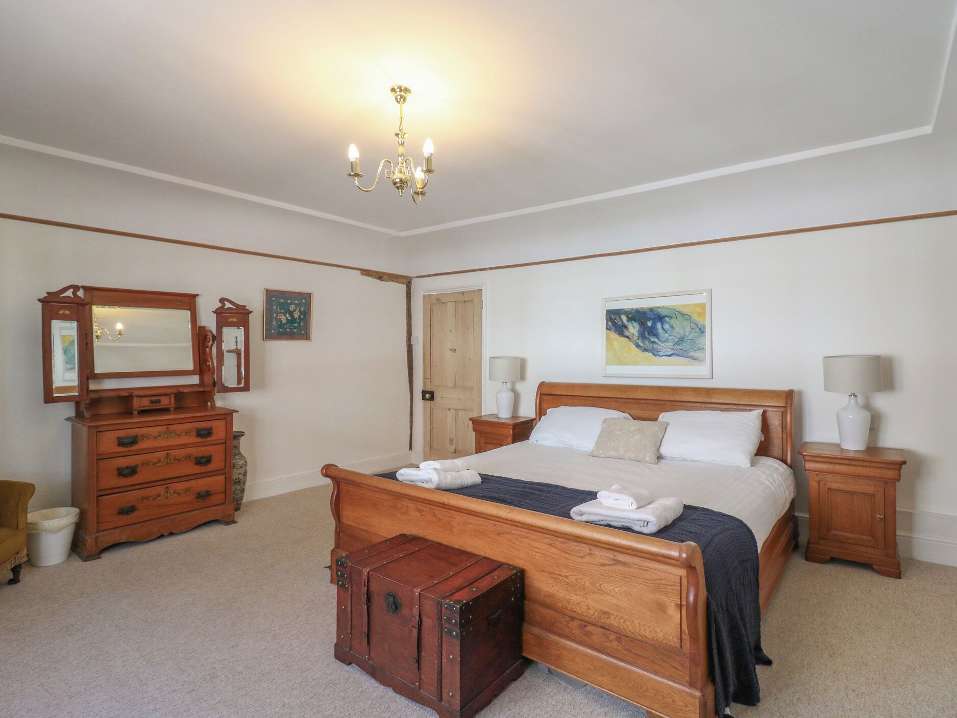 Ein Schlafzimmer mit einem hölzernen Bett, einer Kommode, einem Schminktisch, einem Spiegel und einer Kristallleuchter.