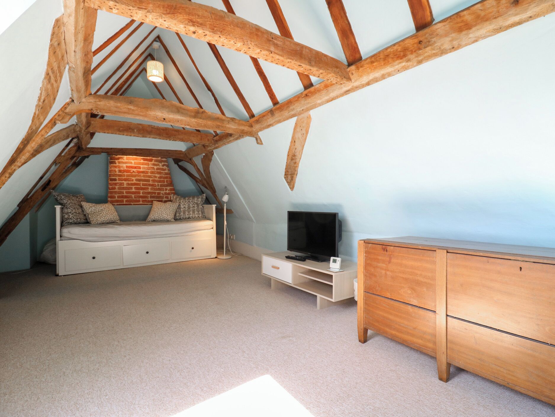 Un dormitorio tipo loft con techo inclinado, una cama, un televisor y un aparador.