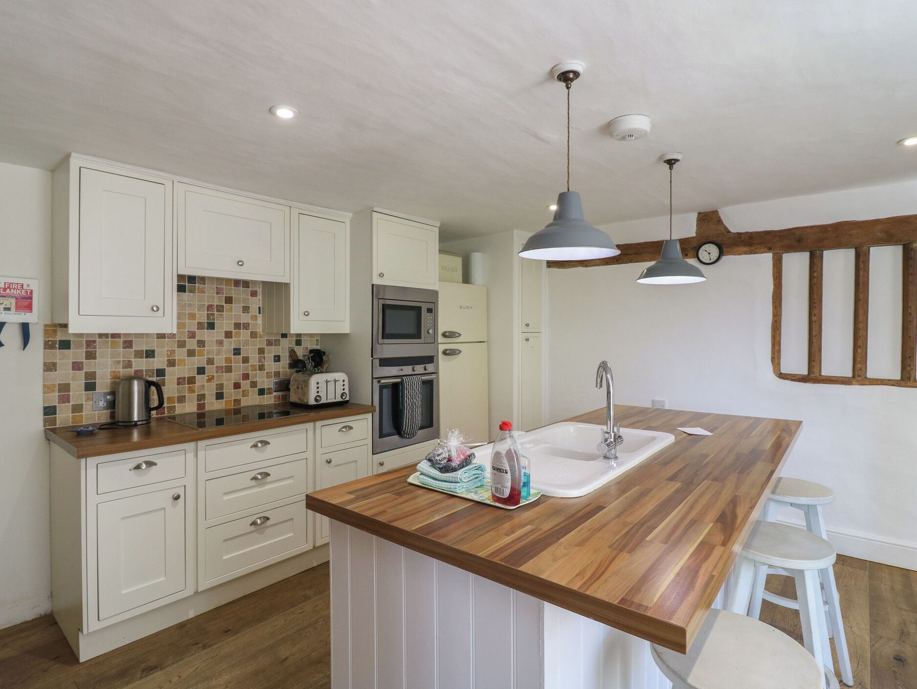 Eine moderne Küche mit weißen Schränken, einer Holz Arbeitsplatte, einem eingebauten Backofen, einer Mikrowelle und einem Spülbecken mit einem hölzernen Hocker.