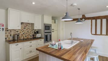 Eine moderne Küche mit weißen Schränken, einer Holz Arbeitsplatte, einem eingebauten Backofen, einer Mikrowelle und einem Spülbecken mit einem hölzernen Hocker.