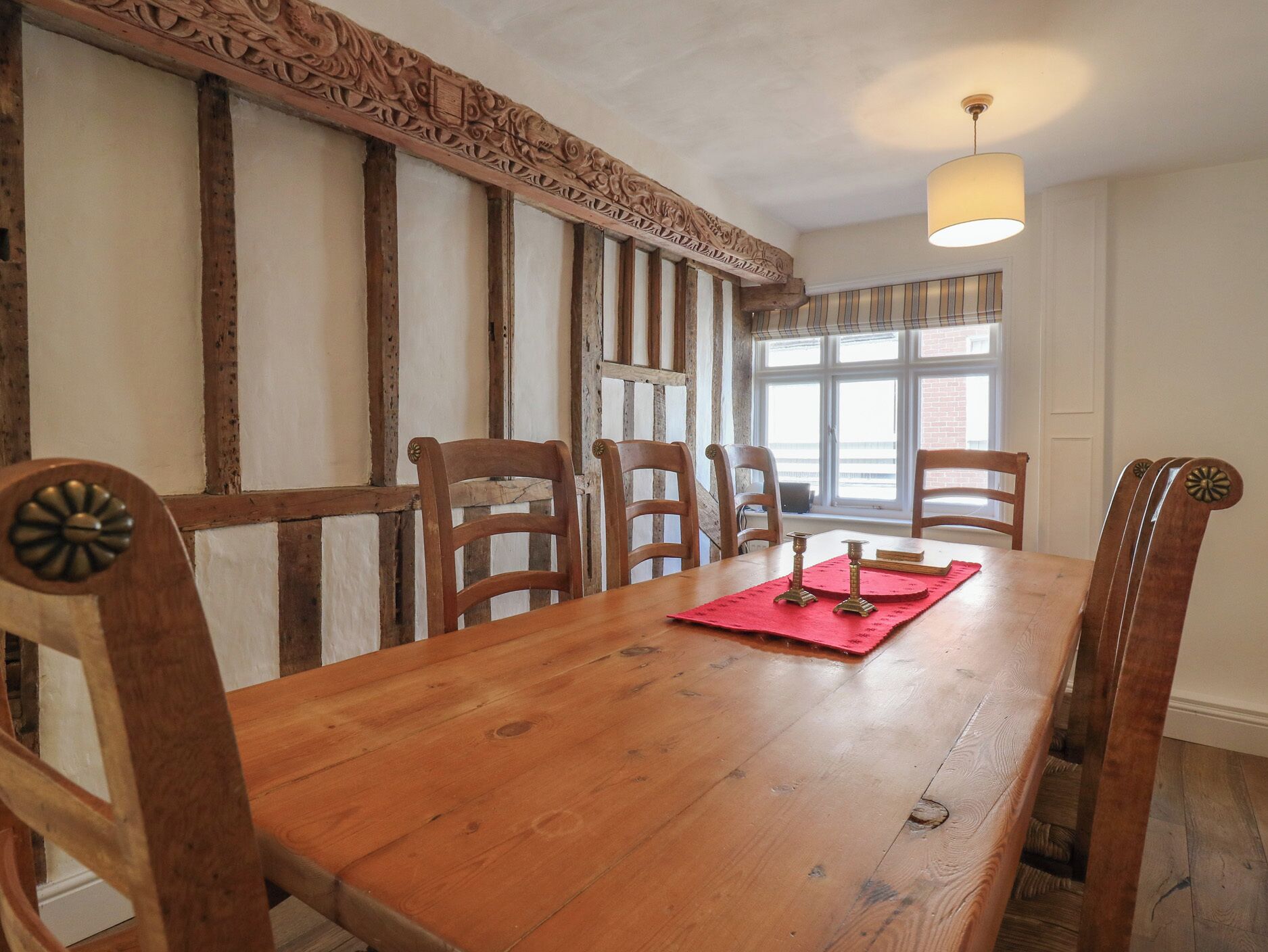 A wooden dining table with six chairs, a red placemat, and candle holders.