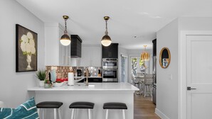 Een moderne keuken met een centraal eiland, barstoelen, hanglampen en een eethoek met stoelen.