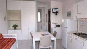A compact kitchen with a dining table, chairs, a microwave, and a stove. - Convenient central apartment (Lignano Sabbiadoro)