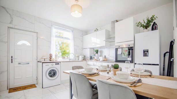 Een moderne keuken met een wasmachine, een eettafel gedekt met borden en glazen, en een koelkast.
