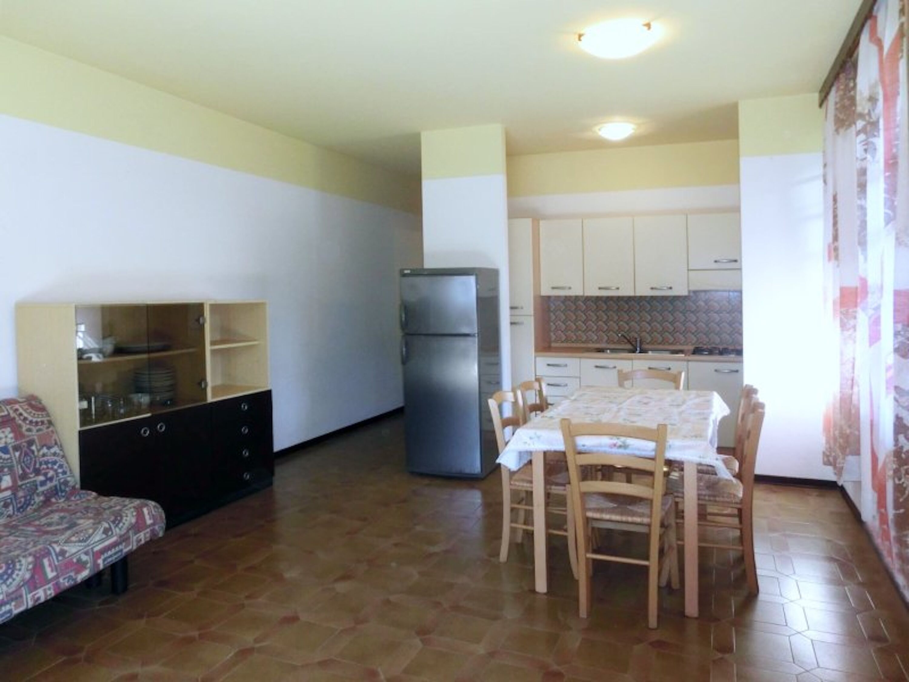 Un espacio habitable compacto con una mesa de comedor, sillas, un sofá, un refrigerador y una cocina con armarios y un salpicadero de azulejos.