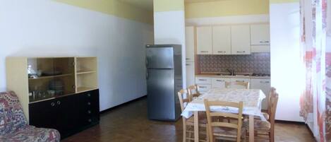 Un espacio habitable compacto con una mesa de comedor, sillas, un sofá, un refrigerador y una cocina con armarios y un salpicadero de azulejos.