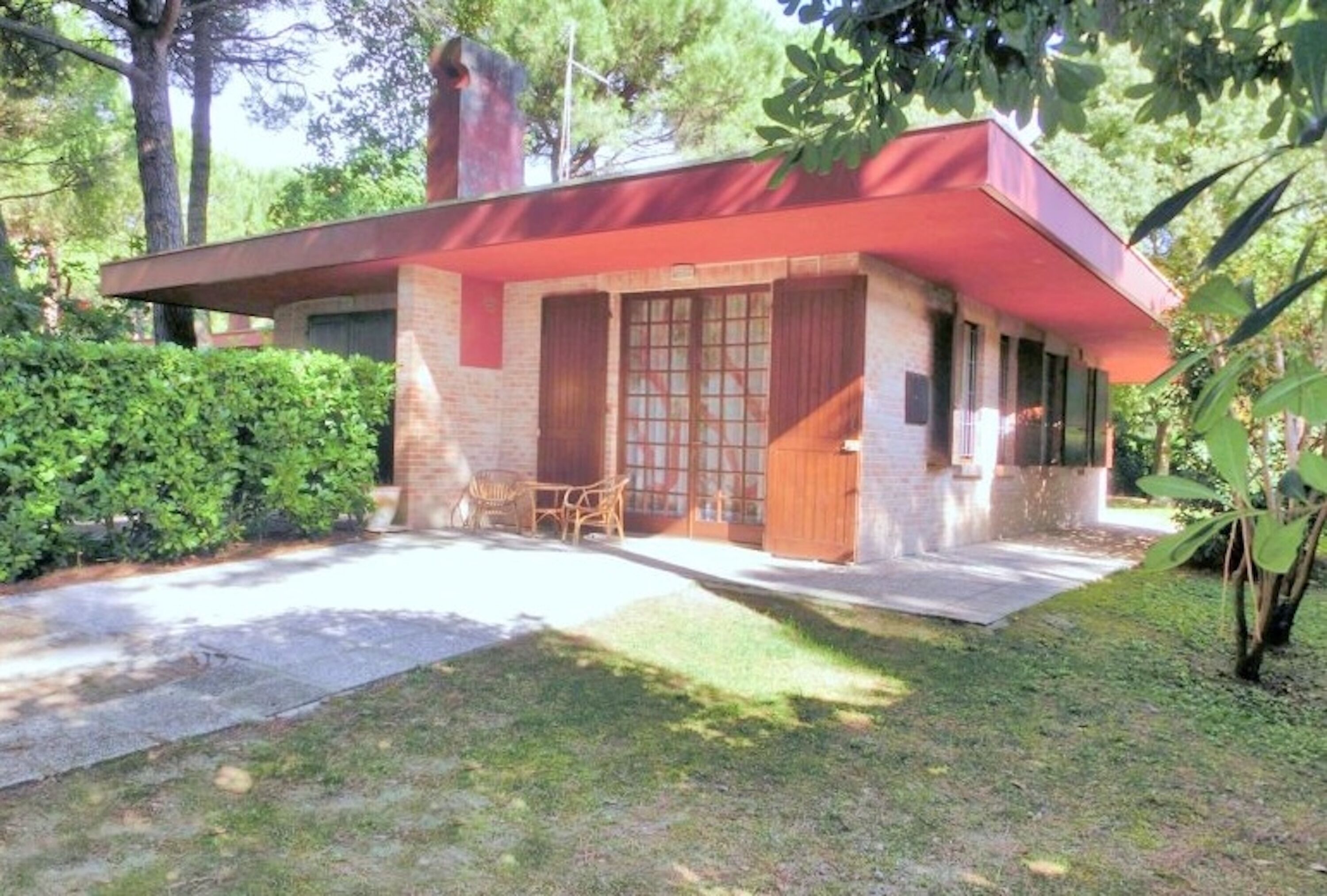 Une maison moderne avec un toit rouge, une façade en briques et un petit patio agrémenté de mobilier d’extérieur.