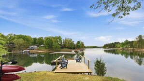 A calm lake with a wooden dock, two chairs, and red kayaks. - Lakefront Retreat • Private Dock + Firepit + Game Room | Montclair Manor (Mooresville)