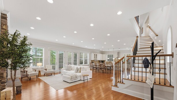 A spacious living area with hardwood flooring, a white sofa set, a dining table, and a staircase with a wooden railing. - Lakefront Retreat • Private Dock + Firepit + Game Room | Montclair Manor (Mooresville)