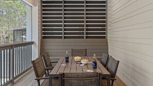 Una terraza de madera con una mesa preparada para cuatro personas, que incluye un cuenco de patatas fritas, dos botellas de cerveza y cartas.