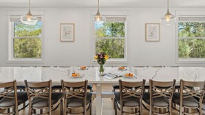 Un comedor moderno con una mesa de mármol, sillas de madera, lámparas colgantes y cuadros en las paredes.