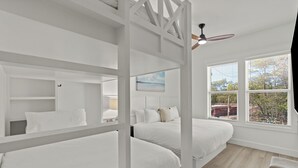 Ein Schlafzimmer mit Etagenbetten, Deckenventilator und einem Fenster mit Jalousien.