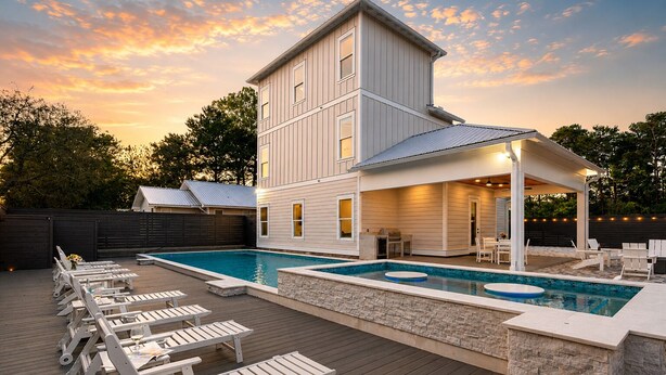 Ein zweigeschossiges Haus mit Pool, Liegestühlen und einer überdachten Terrasse.