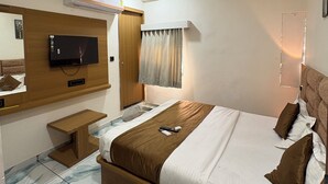 Habitación de hotel con cama, televisión, aire acondicionado, mesita de noche y ventana con cortinas.