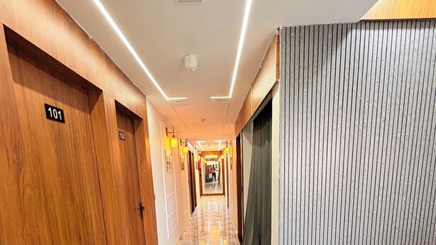 Pasillo de hotel con puertas de madera numeradas 101 y 102, suelo de mármol y un rincón de descanso con sofá y sillón.