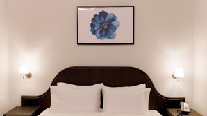 A hotel room with a bed, two bedside tables, a nightstand, a framed picture on the wall, and wall-mounted lamps. - Pana Unique Semey (Semipalatinsk)