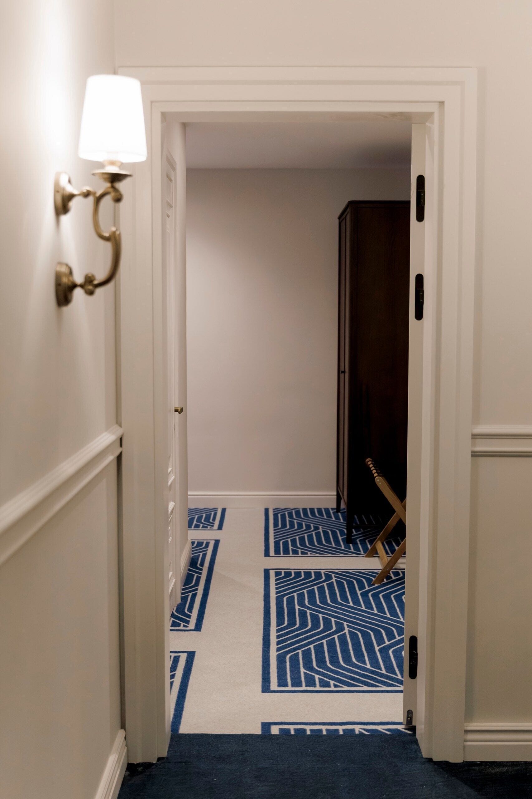 A hallway with a patterned carpet, a wall-mounted light fixture, and a door leading to another room.