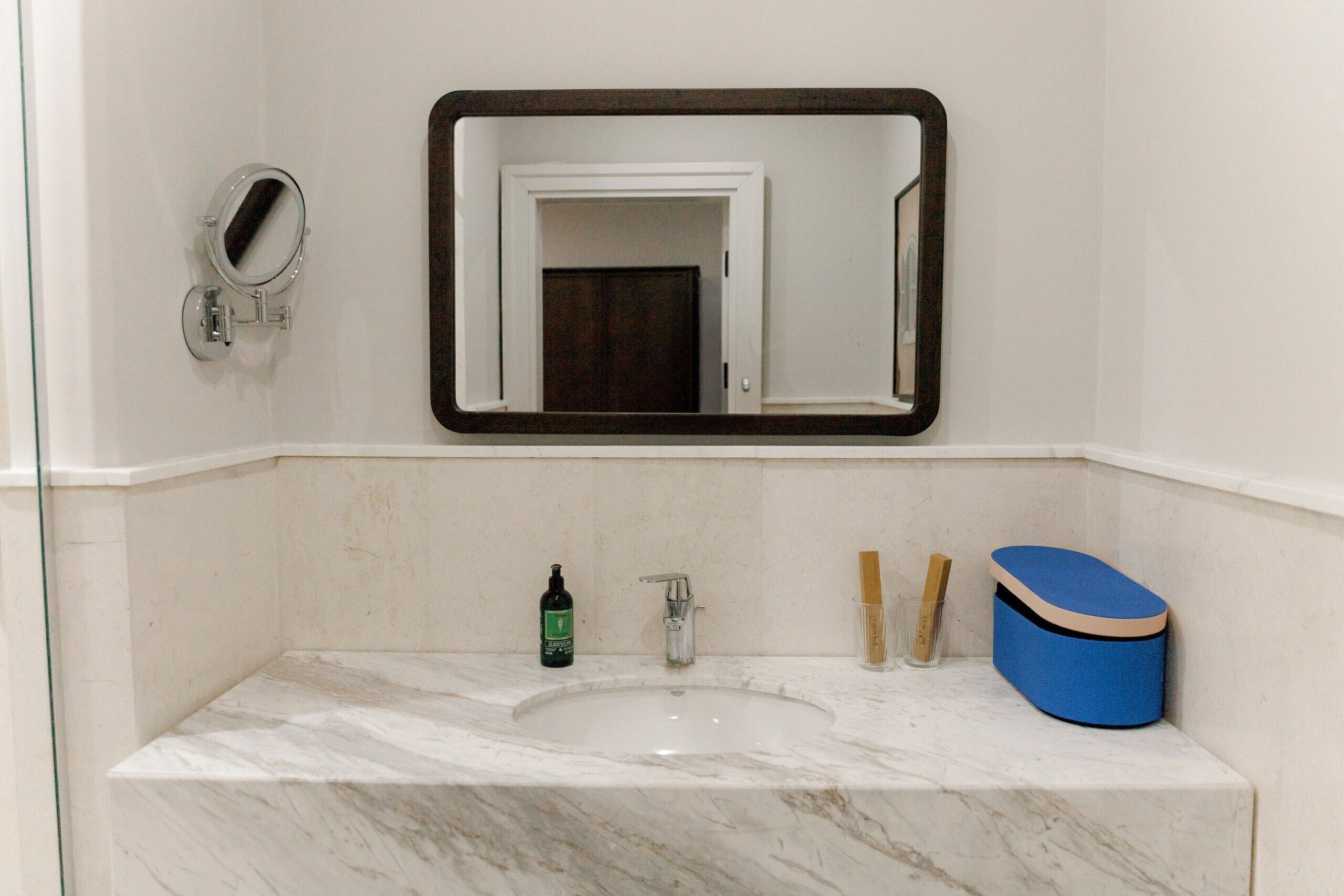 Ein Badezimmer mit einem мраморный Waschbecken, einem Spiegel, einer Seifenflasche und einer blauen Seifenschale.