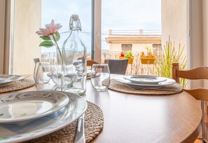 Una mesa de comedor servida con platos, cubiertos y una botella de vidrio con una flor.