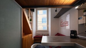 Cocina compacta con una escalera de madera, una ventana con vistas a edificios, un pequeño rincón de descanso y una anexo de cocina.