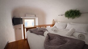 Un dormitorio con cama, televisor montado en la pared, ventana y planta.