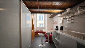 Una cocina estrecha con ventana, un banco rojo, dos taburetes de bar y una cafetera.
