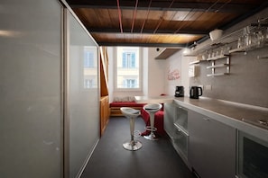 A narrow kitchen with a window, a red bench, two bar stools, and a coffee machine. - Esedra Loft, Like on a Boat Drifting Through Rome (Rome)