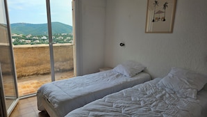 Un dormitorio con dos camas, un ventanal corredero que da a un balcón y un cuadro en la pared.