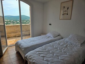Ein Schlafzimmer mit zwei Betten, einer Schiebetür zum Balkon und einem gerahmten Bild an der Wand.