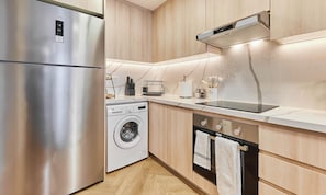 A modern kitchen with stainless steel appliances, a washing machine, wooden cabinets, and a marble backsplash. - bnbme - Lakeside Residence - 1BR (Dubai)