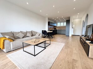 A modern living room with a sofa, coffee table, and kitchen in the background. - Sea view - Large terrace - Walking distance to beaches - Air conditioning - Parking (Bandol)