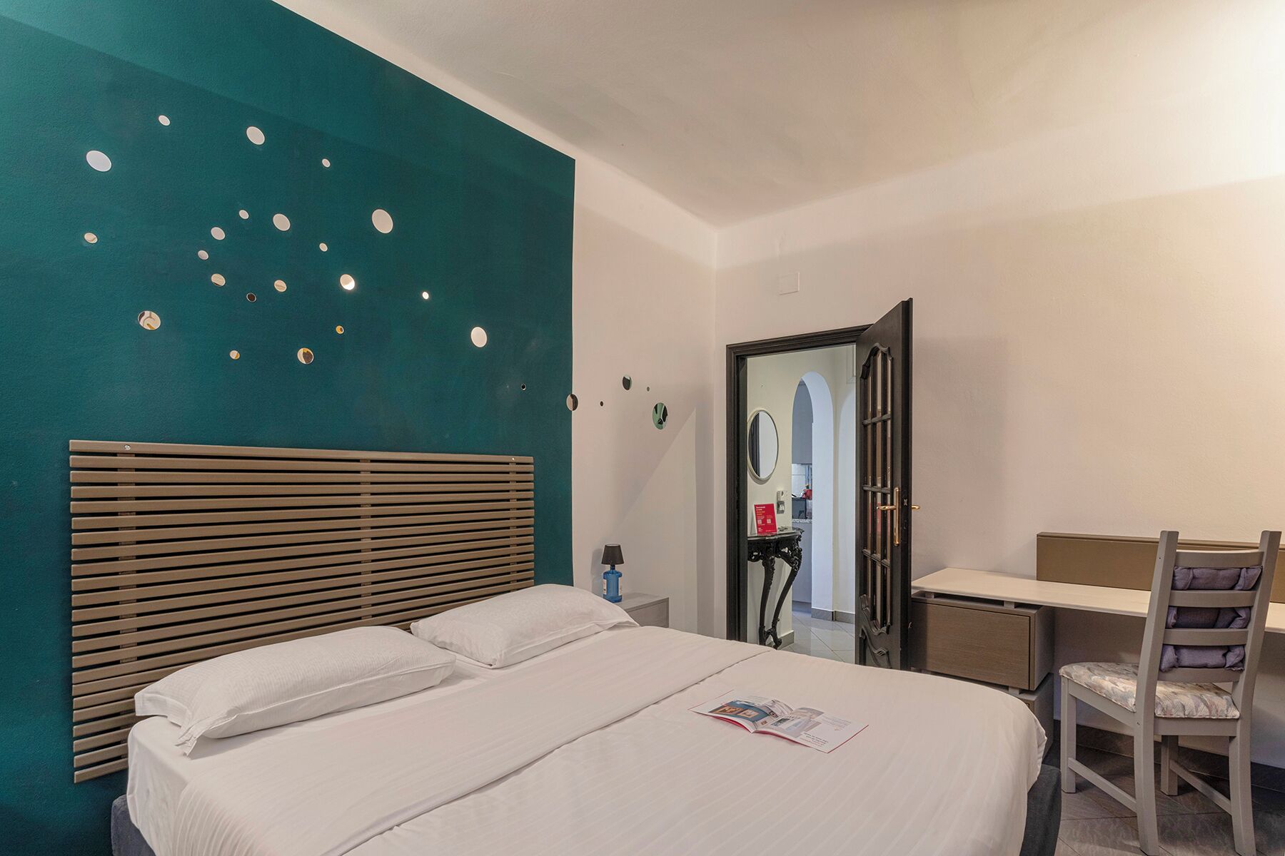 A hotel room with a bed, a desk, a chair, and a mirror.