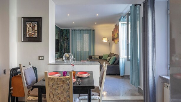 A dining area with a table set for two, a sofa in the background, and a kitchen area visible to the right. - Sweet Coccagna by Wonderful Italy (Genoa)