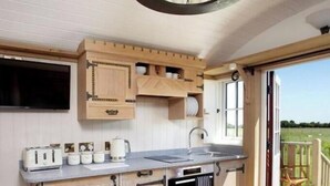 A kitchen with wooden cabinets, a built-in oven, and a large window. - Luxury Shepherd Hut - The White Princess (Bolton Percy)
