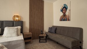A modern hotel room with a bed, a sofa, a small table with a bottle and glass, and a painting on the wall. - Aggire Summer Suites (Zakynthos)