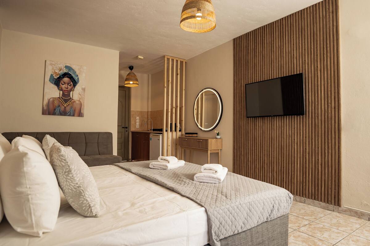 A hotel room with a bed, pillows, a flat-screen TV, a mirror, and a painting on the wall.