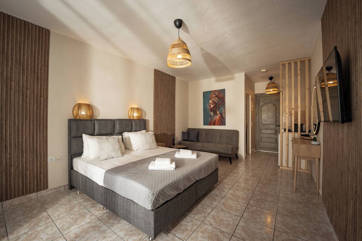 A modern bedroom with a large bed, a sofa, a TV, and a painting on the wall.