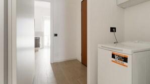 Een wasruimte met een wasmachine, een deur naar een andere kamer en een lichtschakelaar aan de muur.