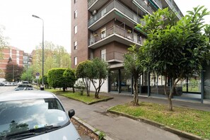 Un edificio a più piani con balconi, un parcheggio e un marciapiede alberato.