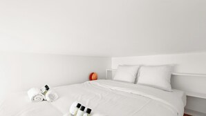 Une chambre d’hôtel au décor minimaliste, comprenant un lit, du linge de lit blanc, une petite table de chevet et des articles de toilette.