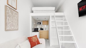 Un espace de vie compact comprenant un lit en mezzanine, une kitchenette et un téléviseur fixé au mur.