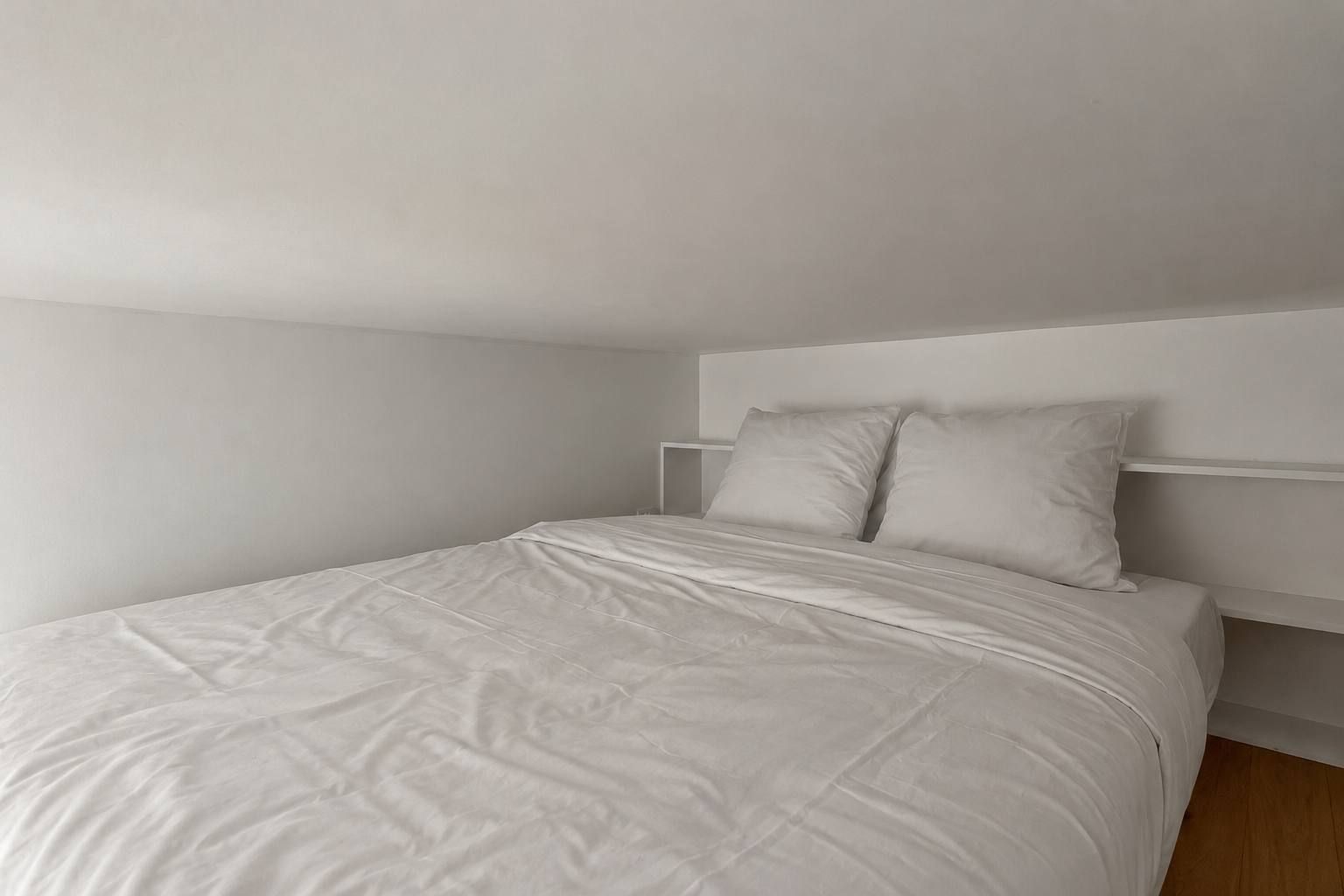 Ein Einzelbett mit weißer Matratze und Kissen, ein weißes Kopfteil und ein Holzboden.