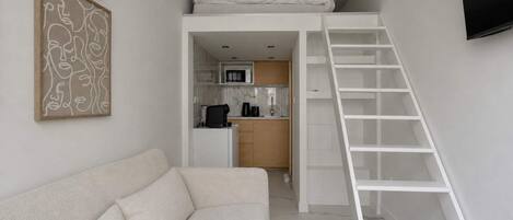Un espace de vie compact comprenant un lit superposé, un coin cuisine et une échelle blanche.