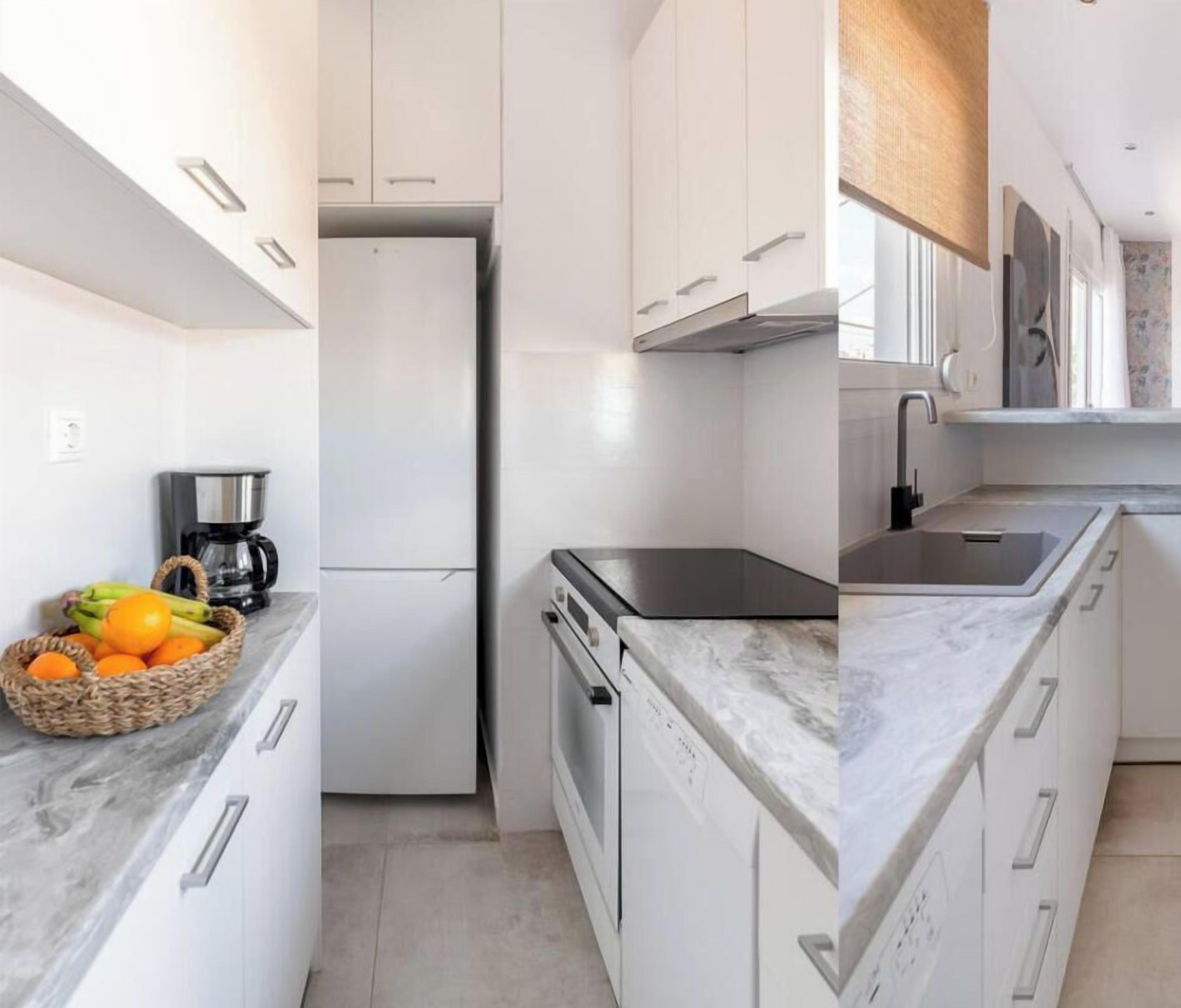 Uma cozinha moderna com armários brancos, forno embutido e bancada de mármore.