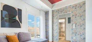 A modern living room with a sofa, a large abstract painting, and a view through a glass door. - Kalypso Acropolis View Rooftop | 6 min to Metro (Athens)