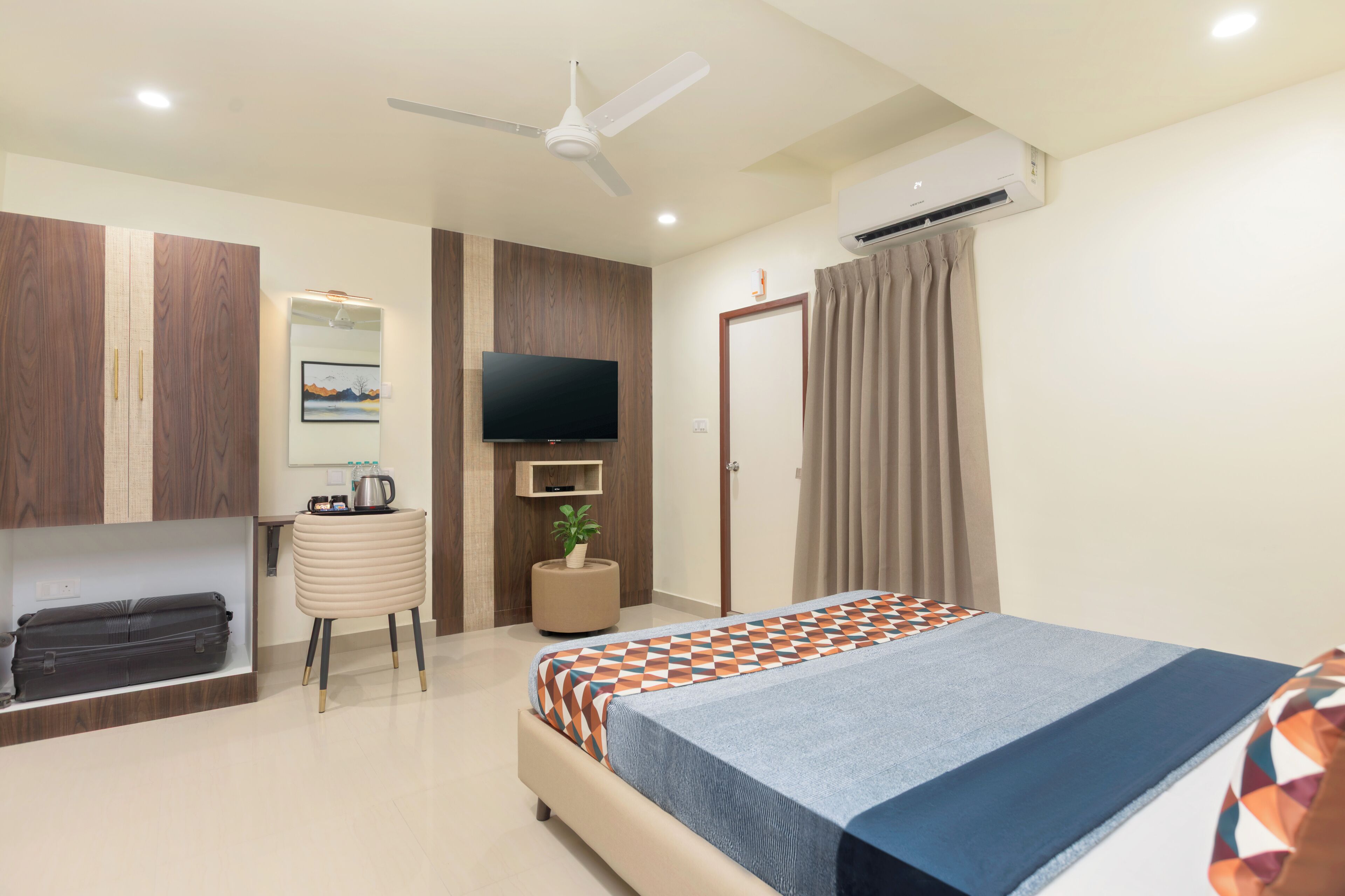 A hotel room with a bed, a desk, a television, an air conditioning unit, and a ceiling fan.