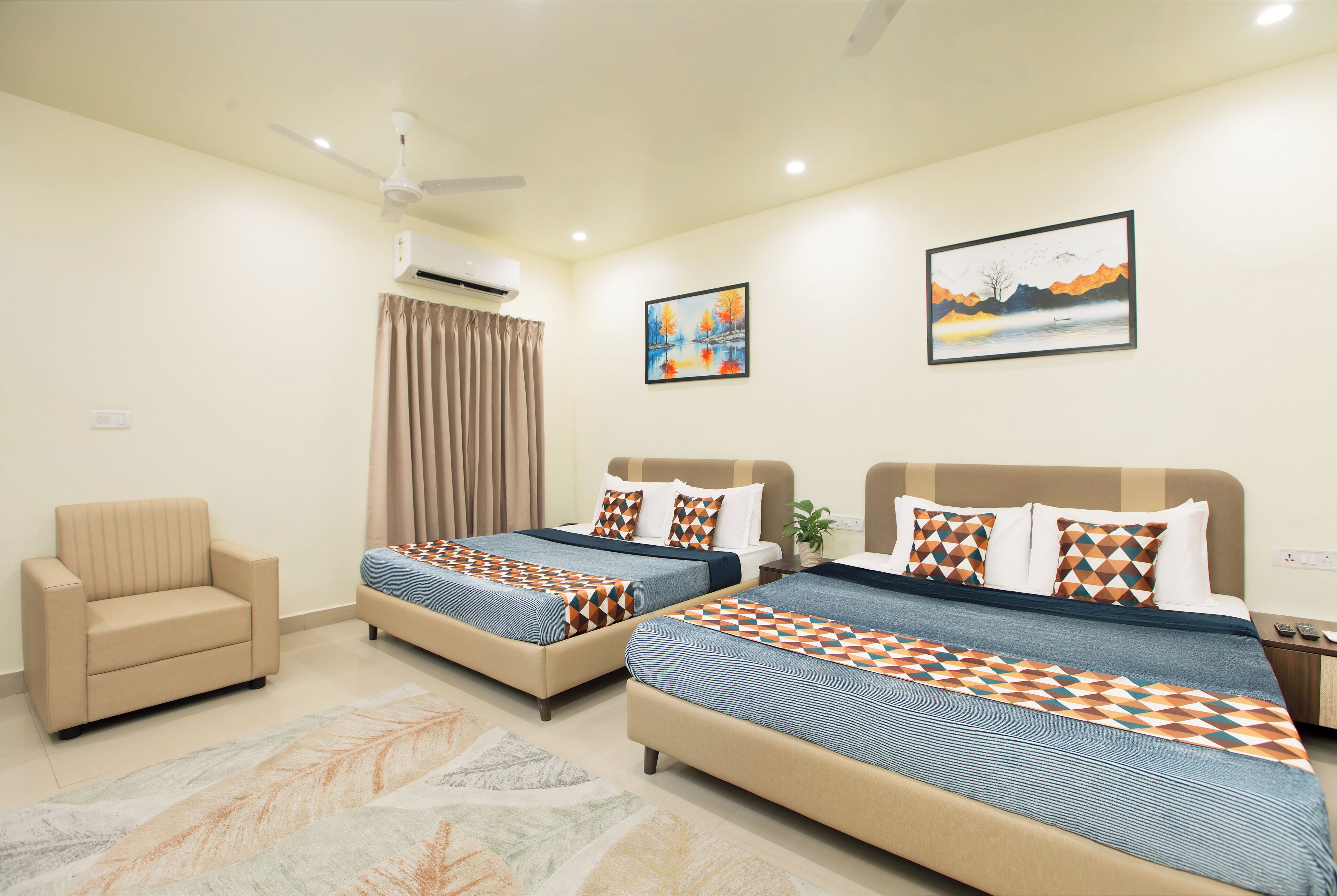 A hotel room with two beds, a chair, an air conditioner, and two paintings on the wall.