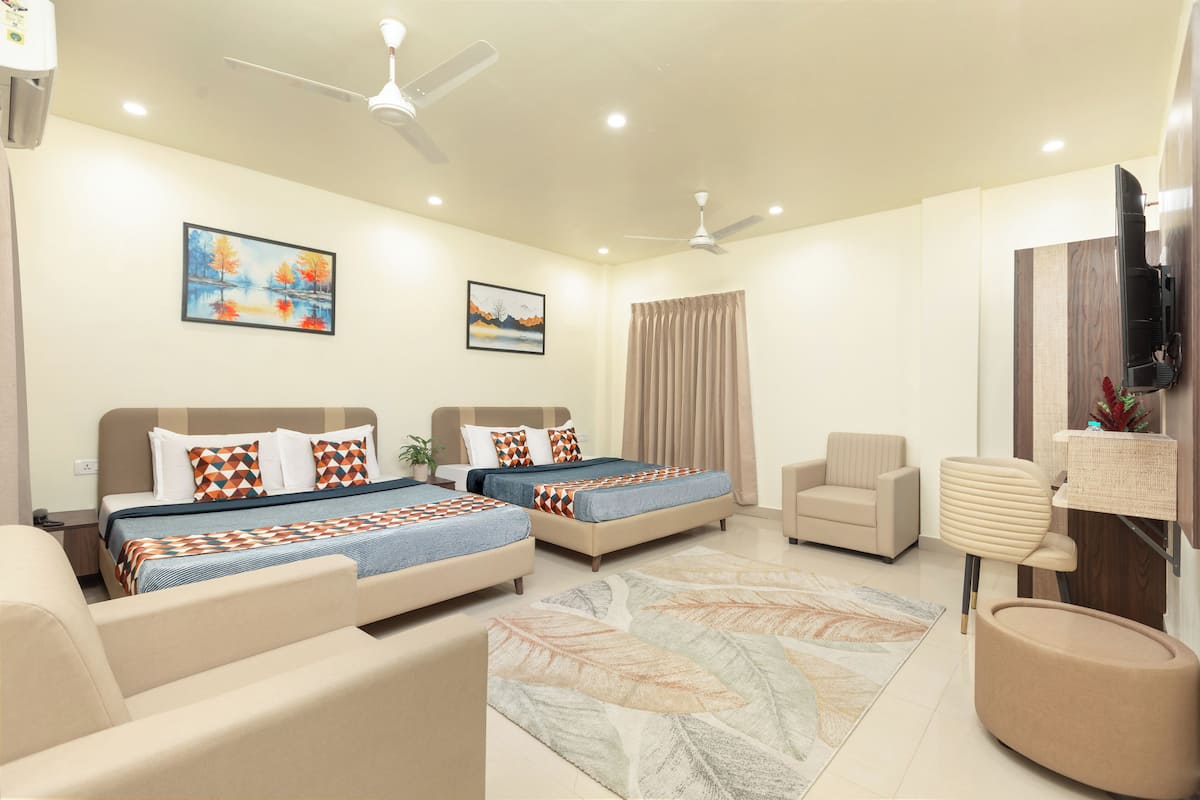 A hotel room with two beds, a sofa, a chair, a TV, and ceiling fans.