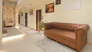 A hallway with a brown leather sofa, a potted plant, and a beige carpet. - Greens Venue (Chennai)